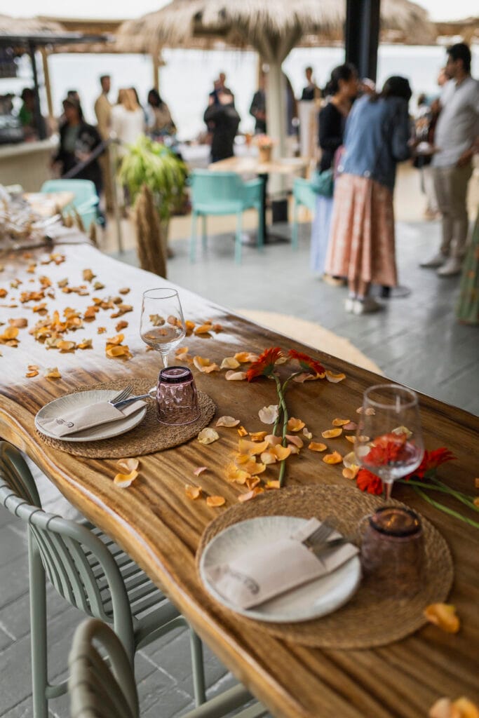 Mesa imperial de madera decorada con pétalos de flores, vajilla y cristalería para una celebración en la terraza de Restaurante Escondida.