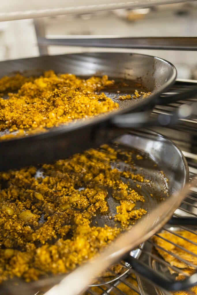 Paellas recién elaboradas en cocina sobre estantes de soporte listas para servir a los invitados en Restaurante Escondida.