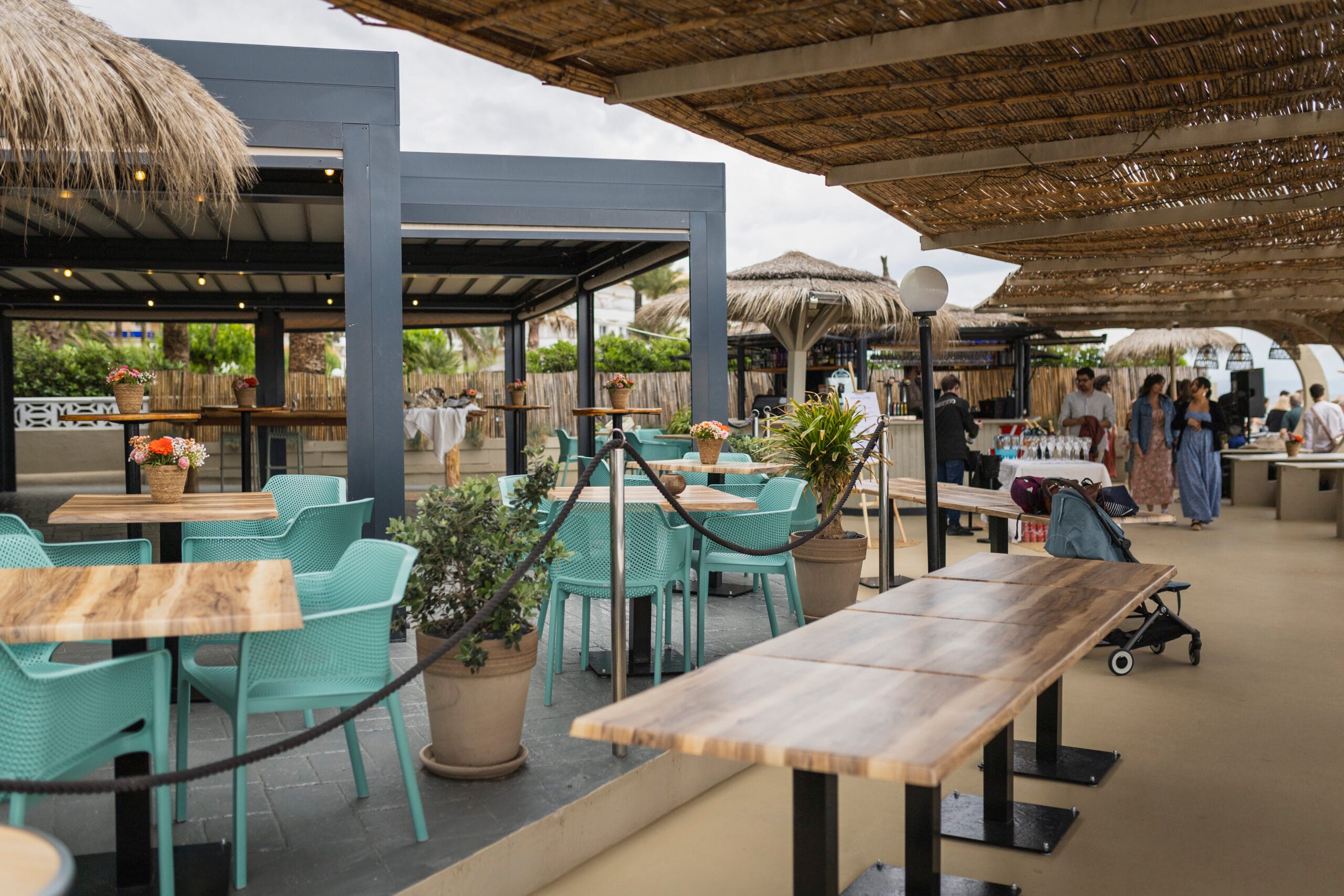 Terraza al aire libre cubierta con techos de paja, mesas de madera y sillas turquesa preparadas para un evento privado en Restaurante Escondida.